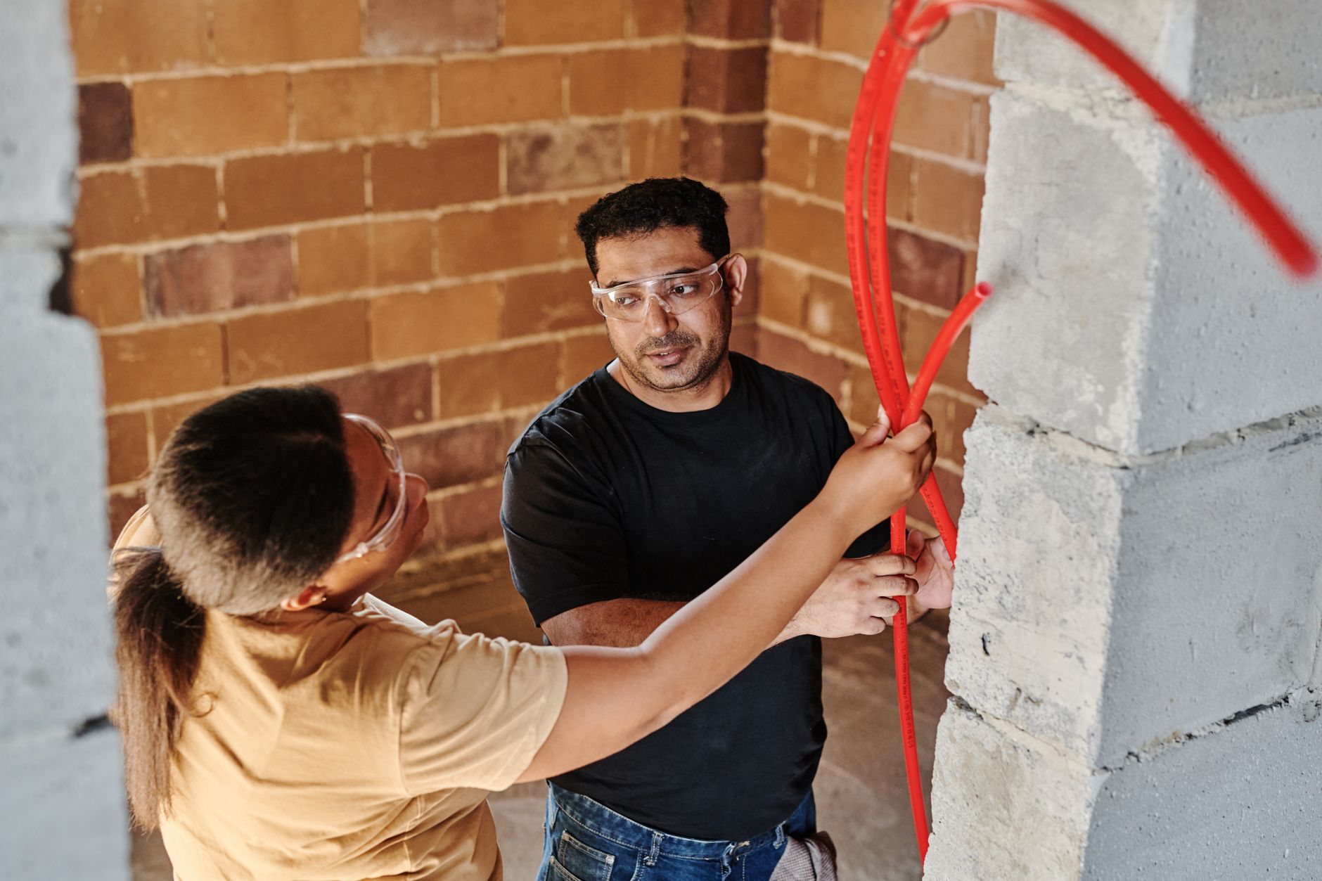 Two workers fitting red tubing at a construction site